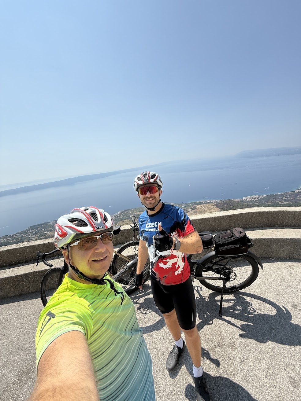 Zwei Radfahrer mit Fahrrädern an einem Aussichtspunkt oberhalb der Küste
